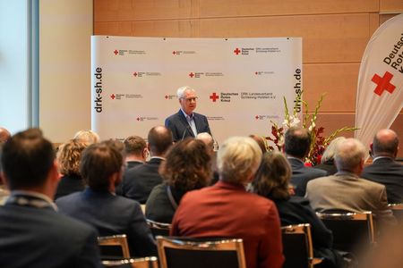 Ein Mann im Anzug steht an einem Rednerpult und spricht zu einigen Menschen.