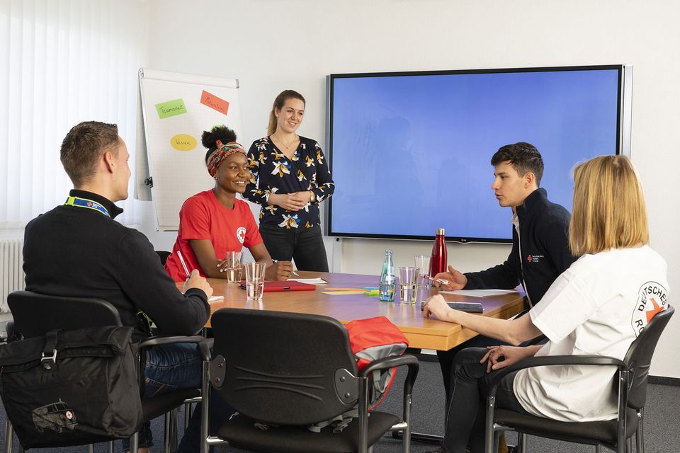 Fünf junge Menschen sitzen an einem Konferenztisch und tauschen sich aus.