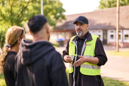Drei Personen unterhalten sich. Eine von ihnen trägt eine gelbe Warnweste mit DRK-Logo.