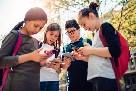 Vier Jugendliche stehen zusammen und beugen sich über ihre Smartphones.